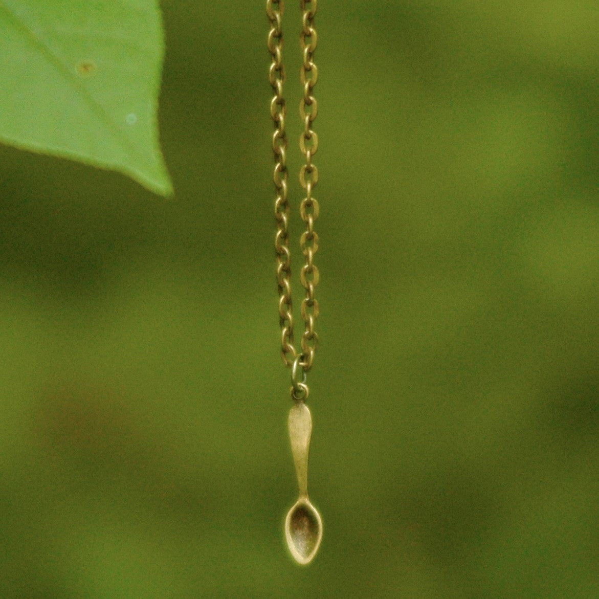 Brass spoon-shaped pendant on a necklace chain.