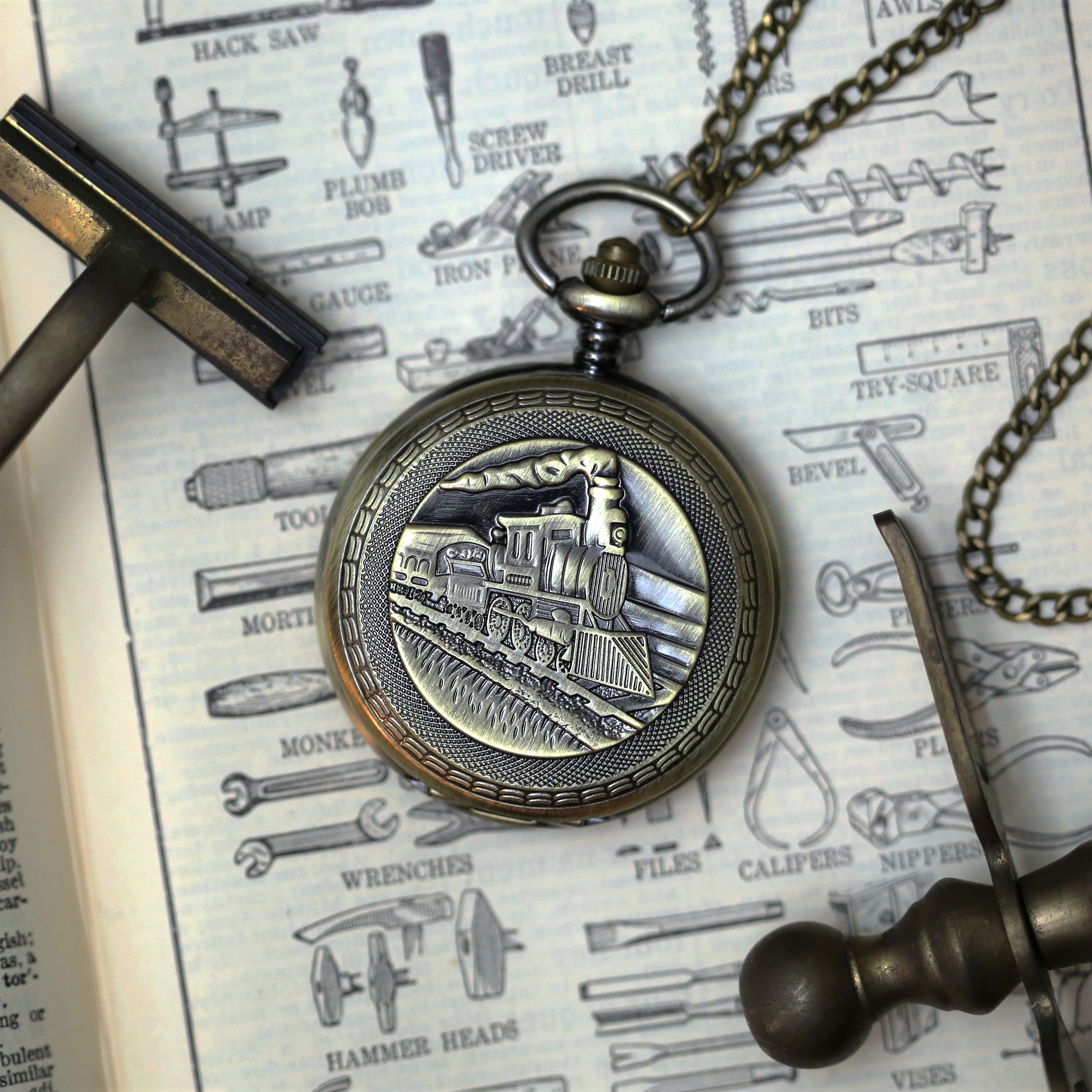 Antiqued brass mechanical pocket watch with a train design on the front, attached to a brass pocket chain.