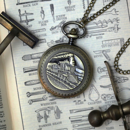 Antiqued brass mechanical pocket watch with a train design on the front, attached to a brass pocket chain.