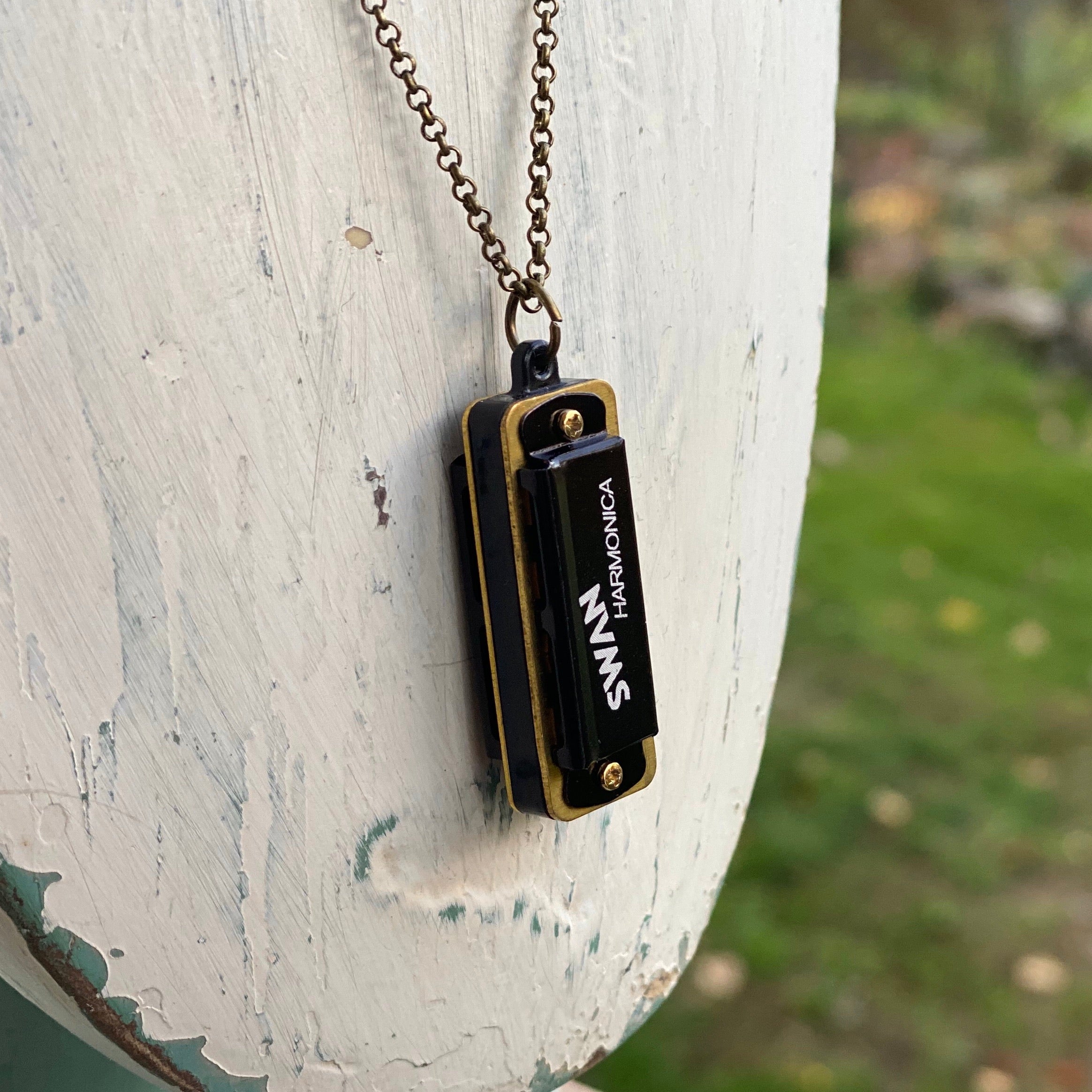 Miniature black SWAN harmonica on a brass chain.