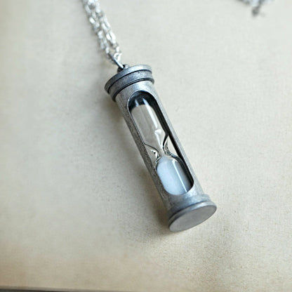 A functional hourglass in an antiqued silver frame hanging from a silver chain. The sand timer's sand is white.