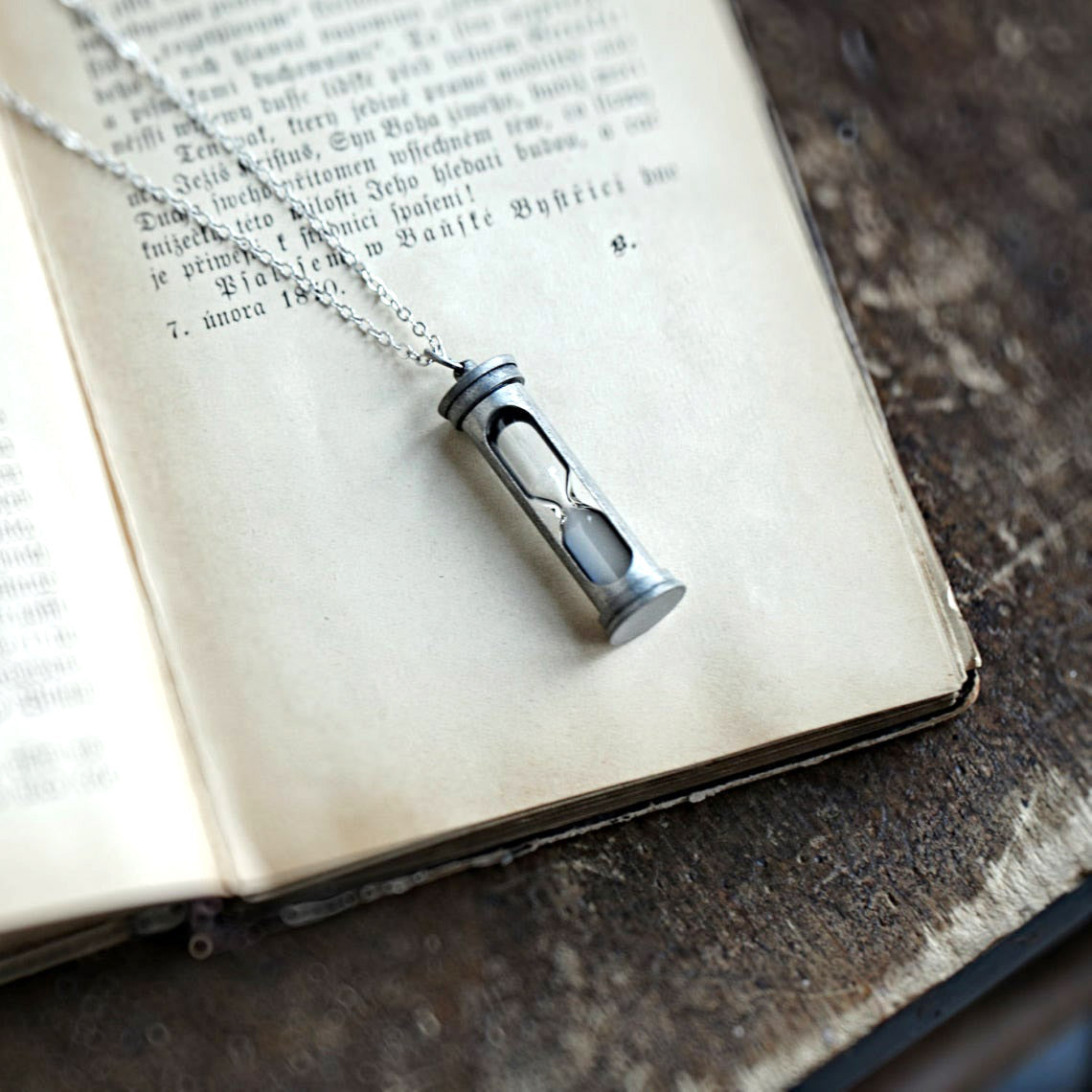 A functional hourglass in an antiqued silver frame hanging from a silver chain.