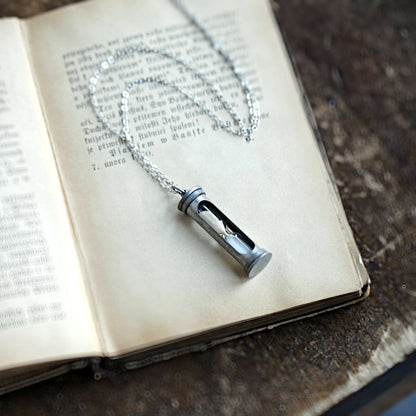 A functional hourglass in an antiqued silver frame hanging from a silver chain.