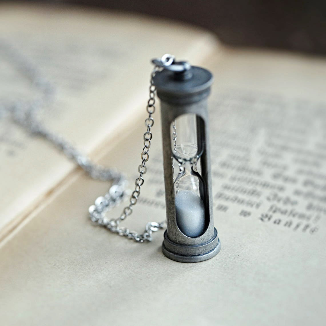 A functional hourglass in an antiqued silver frame hanging from a silver chain.