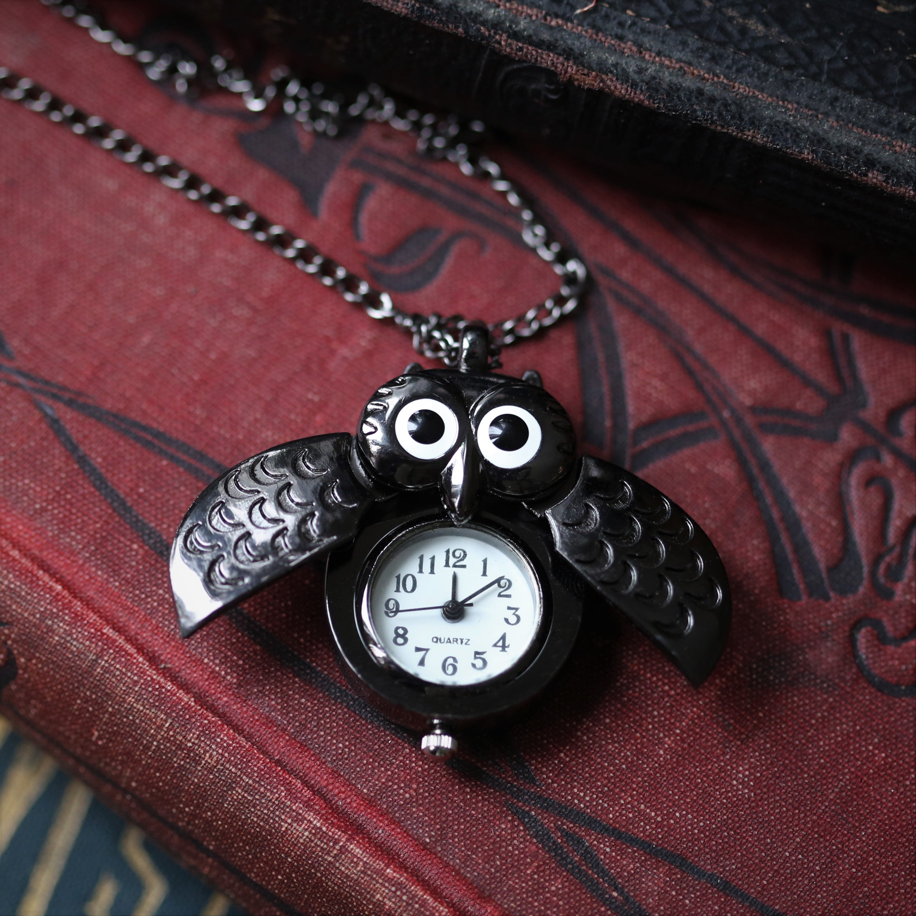 A gun metal owl-shaped watch necklace with a quartz face. This watch is displayed open, with the owl's wings open to show the watch face.