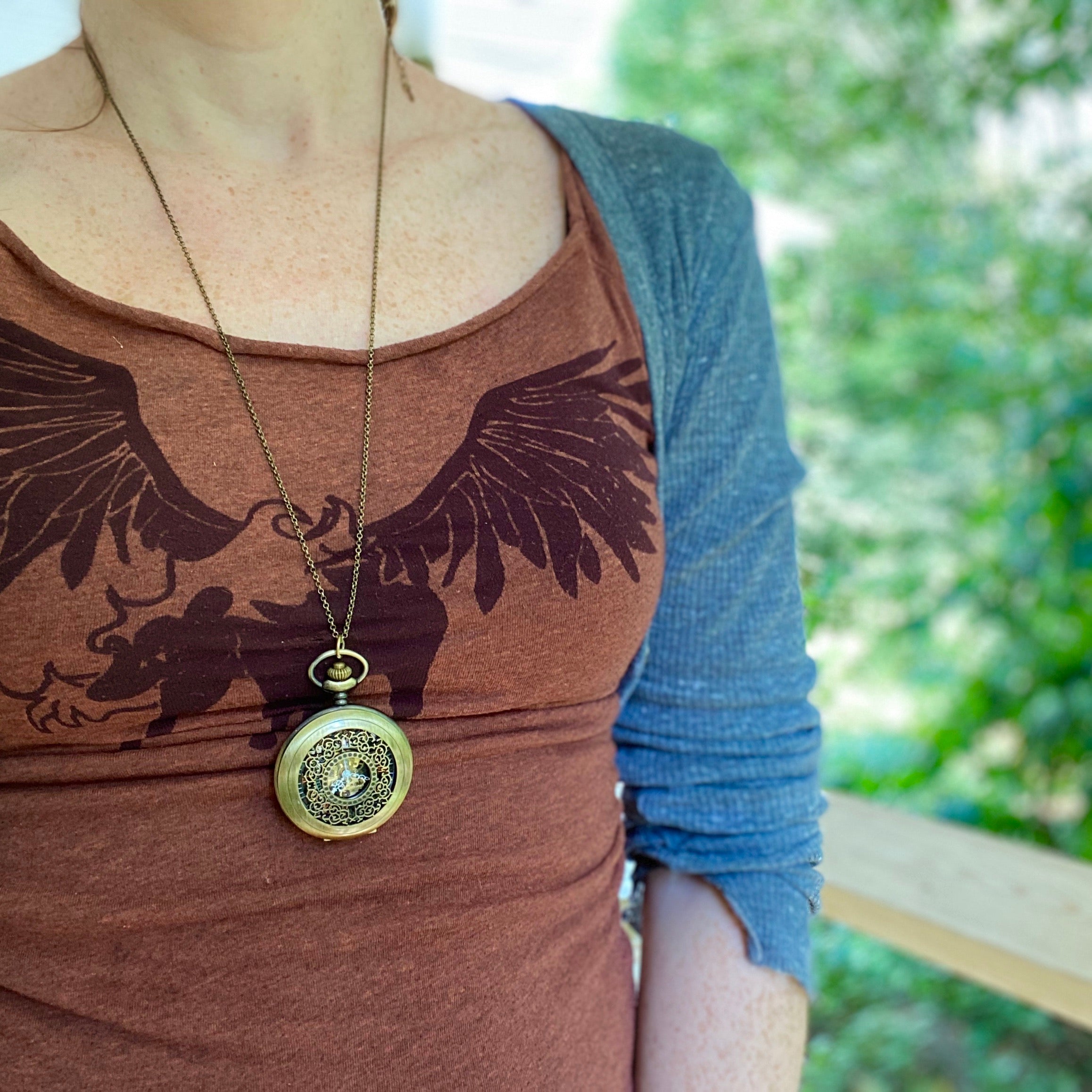 Antiqued brass mechanical pocket watch with intricate designs on the watch cover, displayed on a brass necklace chain.