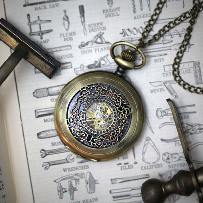 Antiqued brass mechanical pocket watch with intricate designs on the watch cover, displayed on a brass necklace chain.