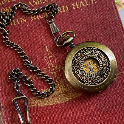 Antiqued brass mechanical pocket watch with intricate designs on the watch cover, displayed on a brass pocket chain.