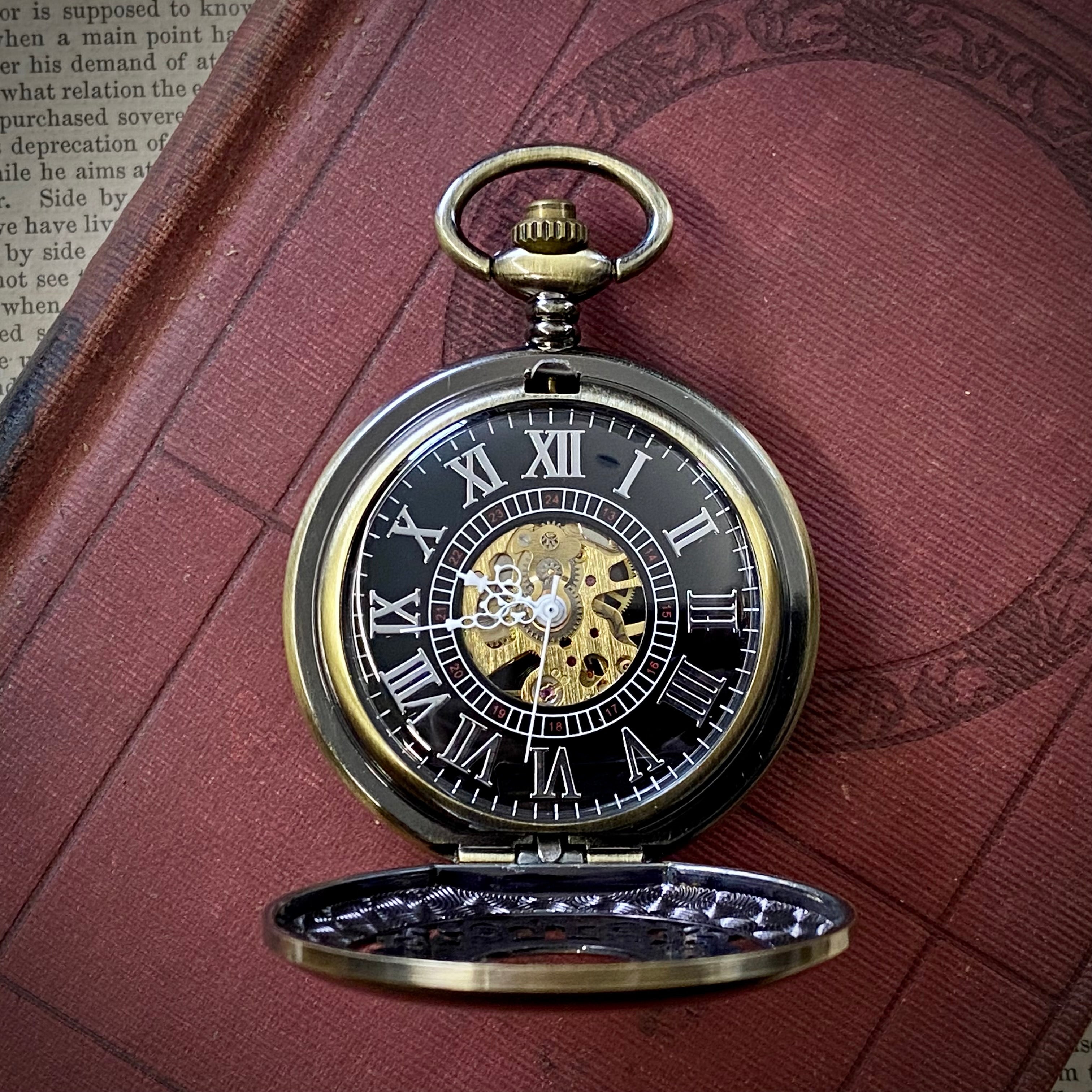 Brass mechanical watch displayed open, with white roman numerals on a black boarder. Watch internal gears are visible through a window in the center of the watch.