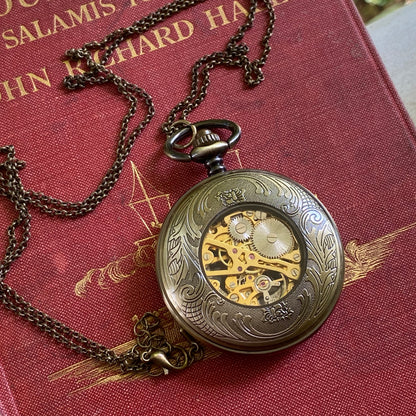 Antiqued brass Cogwheel mechanical pocket watch face down to display an ornate back panel with a window to internal gears in the center.