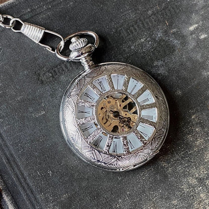 Silver mechanical pocket watch with a cogwheel design on the front, attached to a silver watch chain. The watch is closed, but internal gears are visible through the lid.