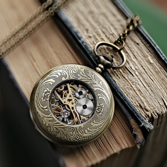 Antiqued brass pocket watch displaying the back. The back of the watch has a window to the internal gears.