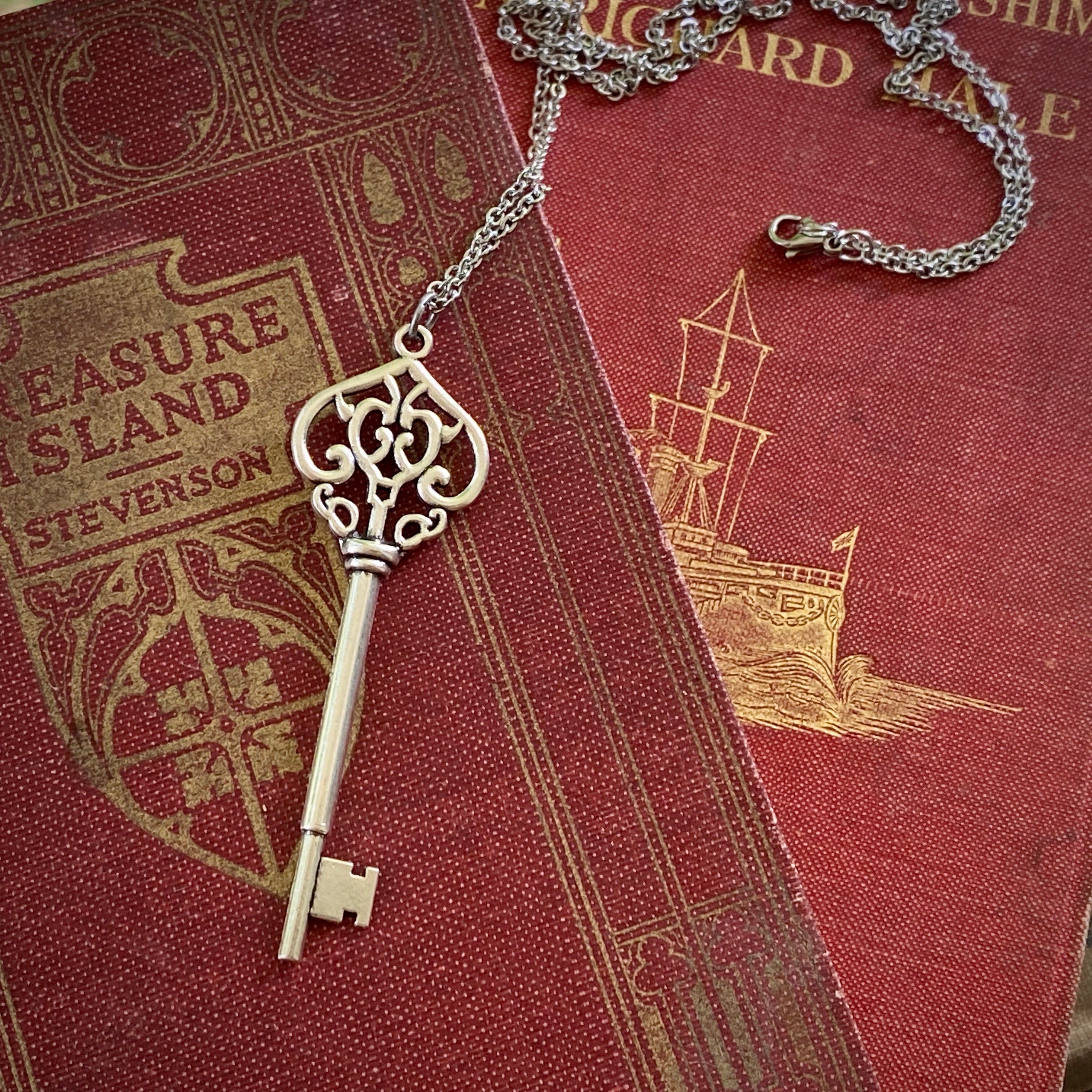 Antiqued brass key pendant necklace. The head of the key is shaped like an ornate upside down heart with two 'c's facing each other inside.