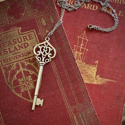 Antiqued brass key pendant necklace. The head of the key is shaped like an ornate upside down heart with two 'c's facing each other inside.