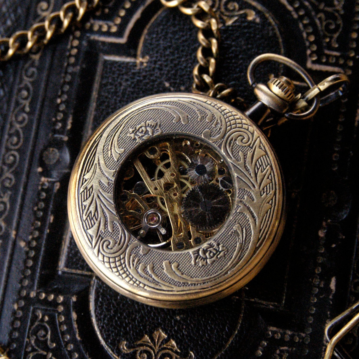 Antiqued brass Zodiac mechanical pocket watch face down to display an ornate back panel with a window to internal gears in the center.