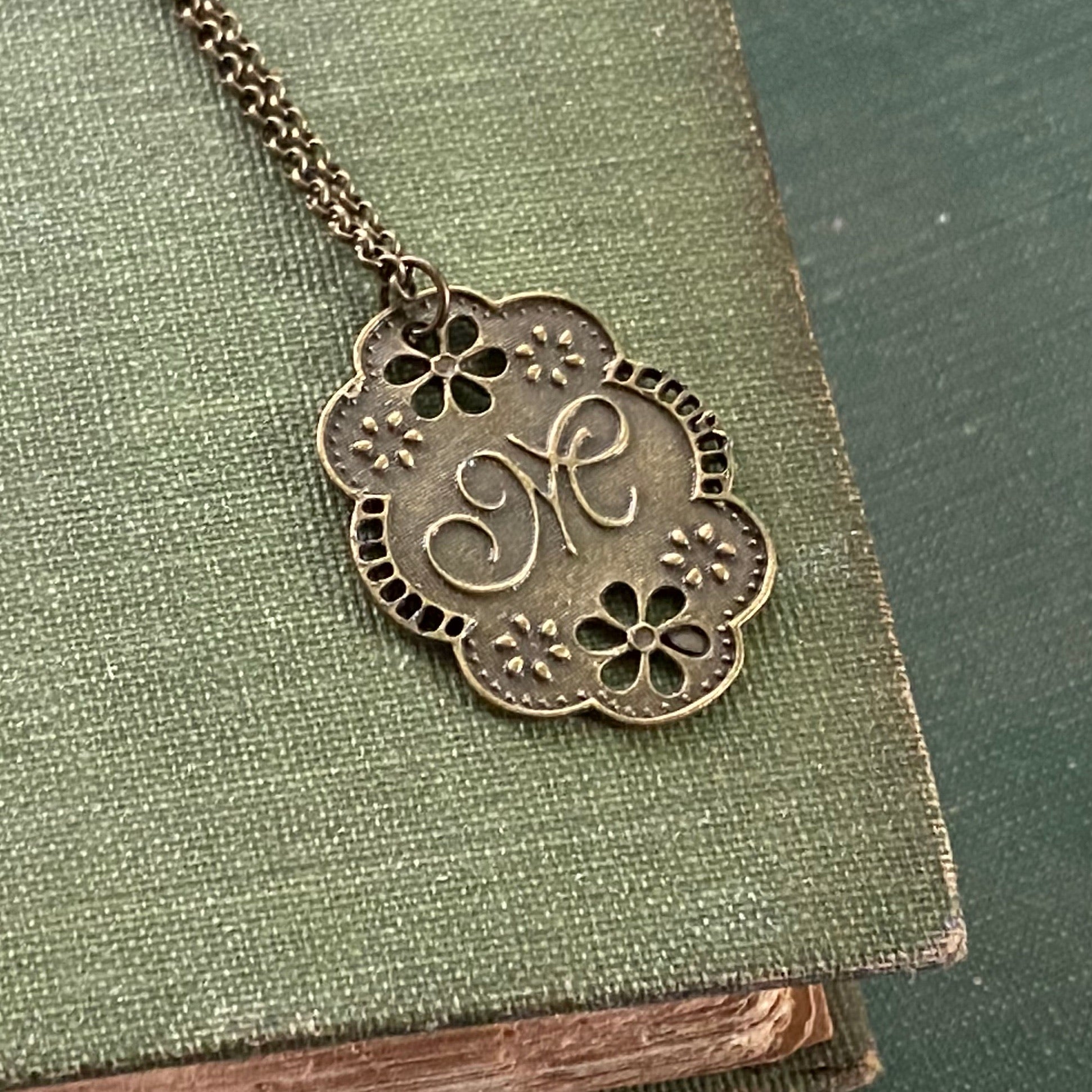 Antique bronze cursive M-initial charm necklace with floral design.