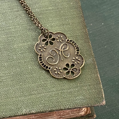 Antique bronze cursive M-initial charm necklace with floral design.