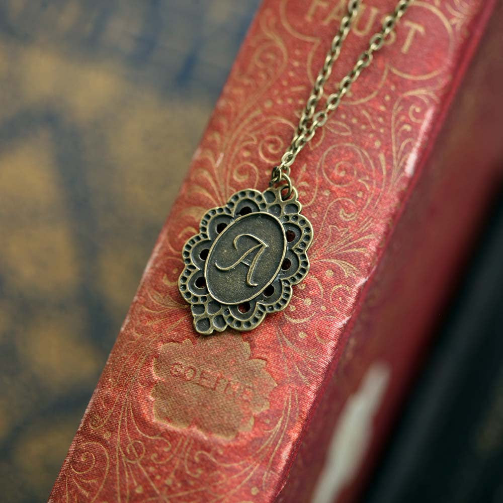 Antiqued brass letter 'A' pendant with an ornate border. The pendant is roughly oval shaped.