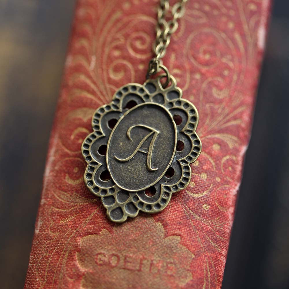 Antiqued brass letter 'A' pendant with an ornate border. The pendant is roughly oval shaped.