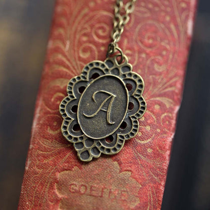 Antiqued brass letter 'A' pendant with an ornate border. The pendant is roughly oval shaped.