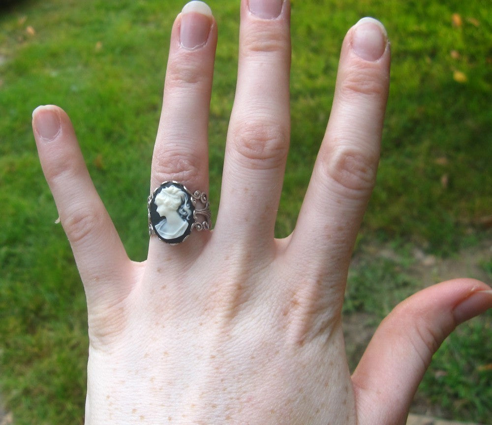 A cameo ring with a white woman on a black background. This oval cameo is set on an adjustable silver filigree ring.