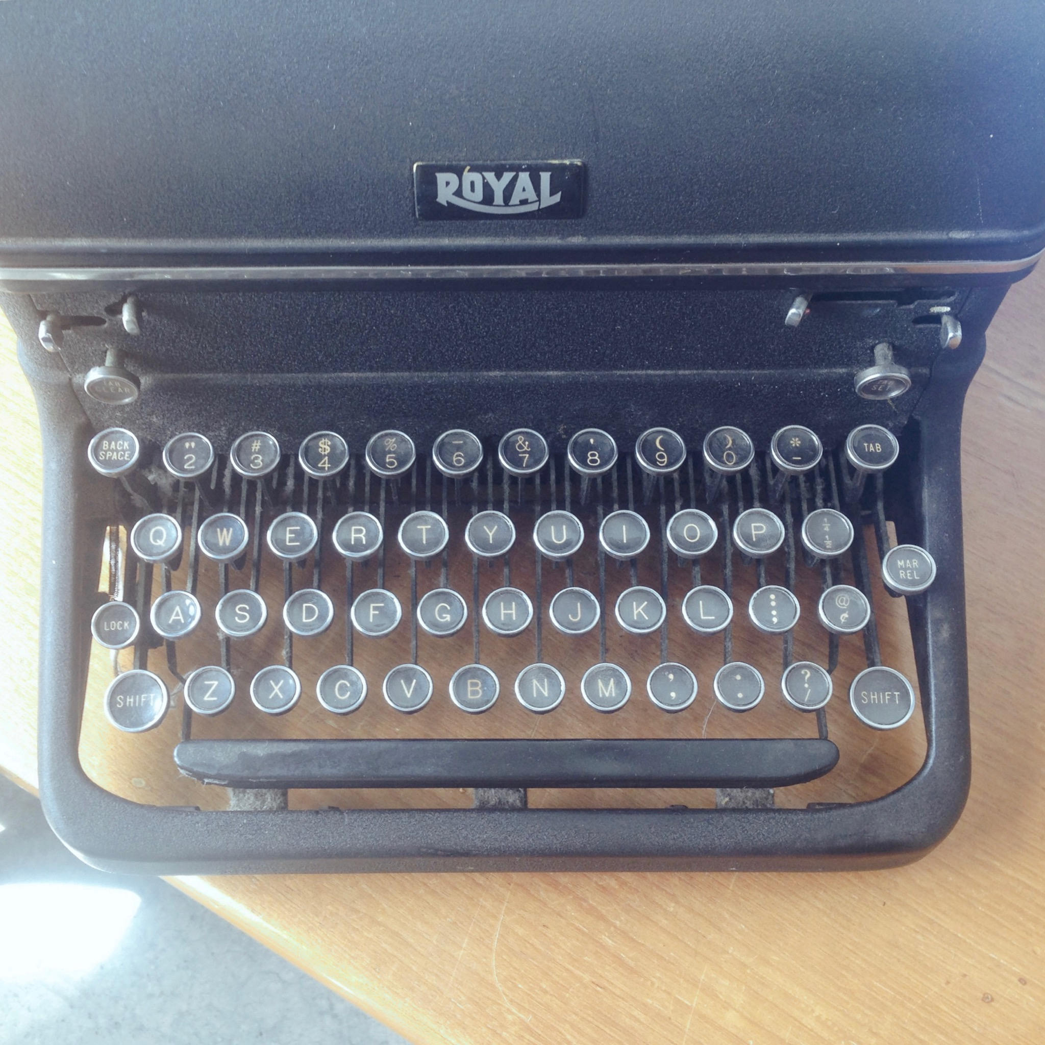 Antique typewriter with keys that are metal-rimmed glass covering off-white letters on black background.