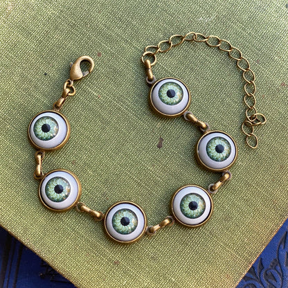 antiqued brass bardcore style adjustable green evil eye charm dangle bracelet.