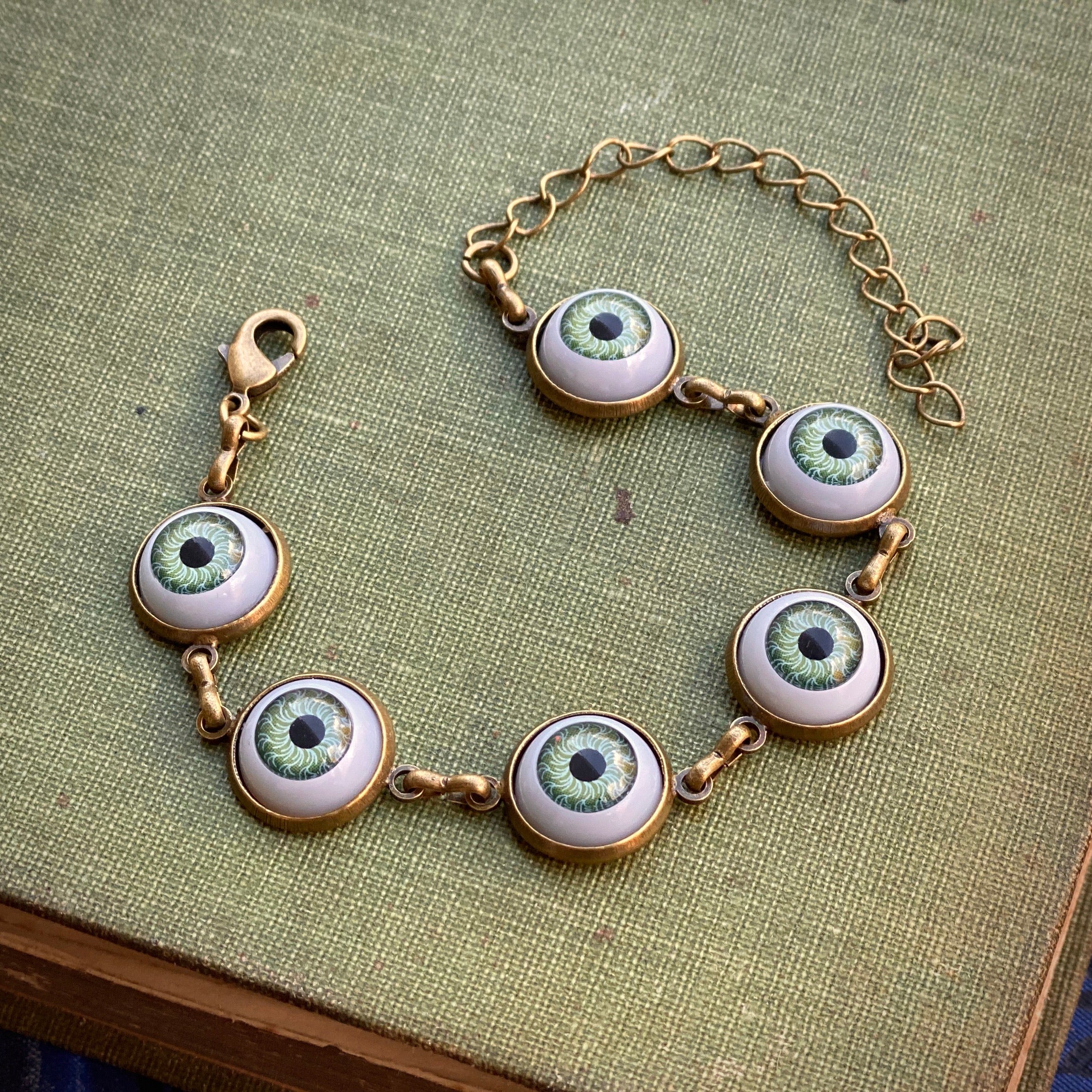 antiqued brass cryptidcore style adjustable green evil eye charm dangle bracelet.