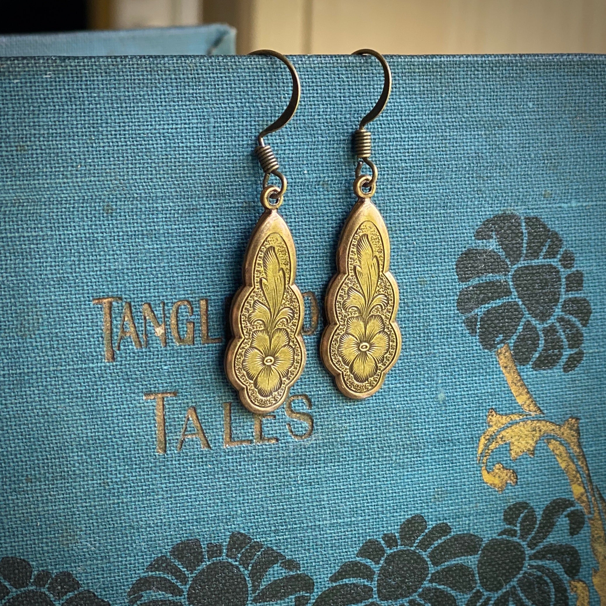 Antiqued brass drop earrings with a floral design.
