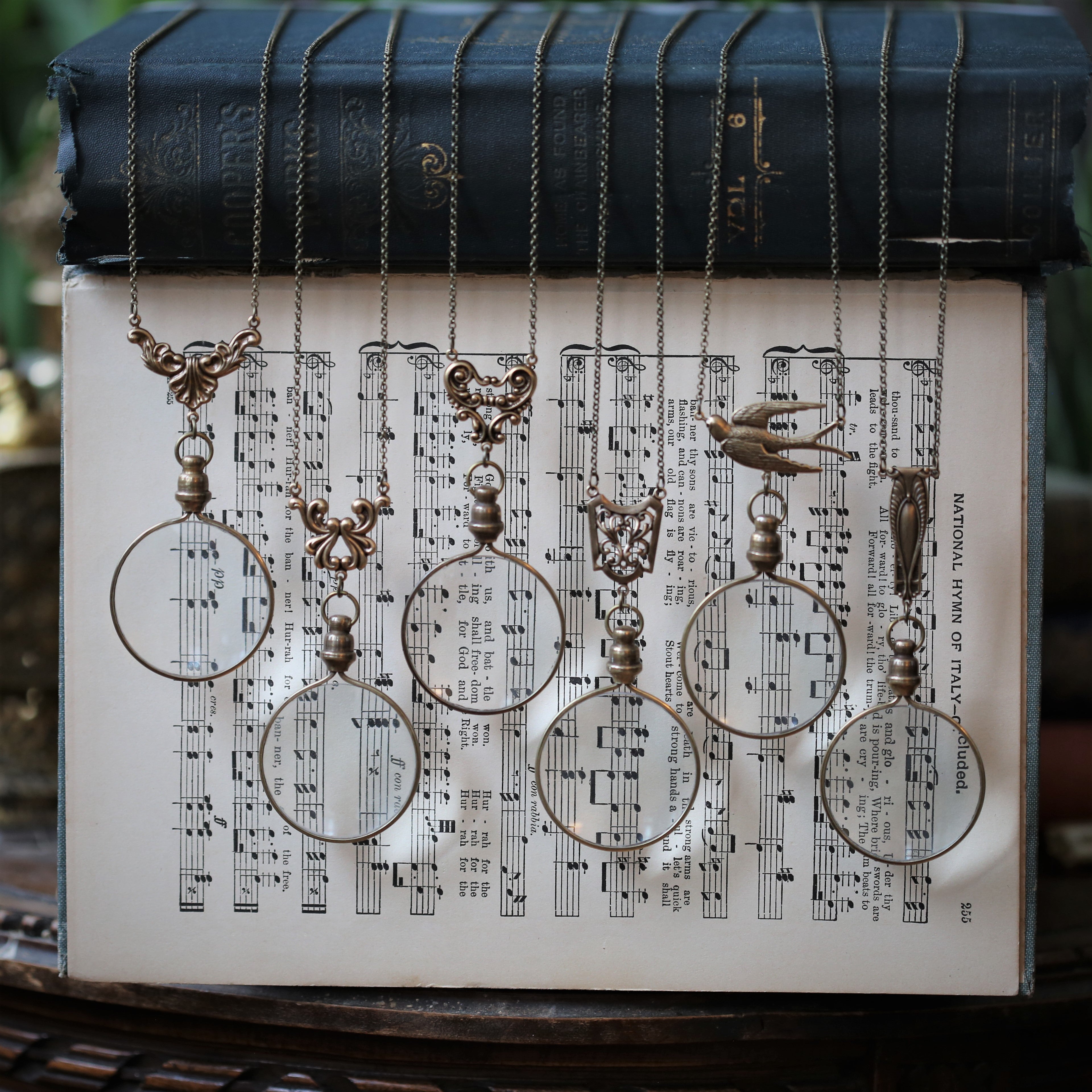 The six brass magnifying glass options side by side. Leaf flourish, swan wing, angel wing, shield lattice, sparrow, and art deco.