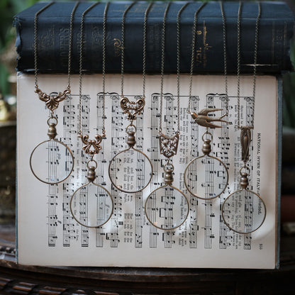 The six brass magnifying glass options side by side. Leaf flourish, swan wing, angel wing, shield lattice, sparrow, and art deco.