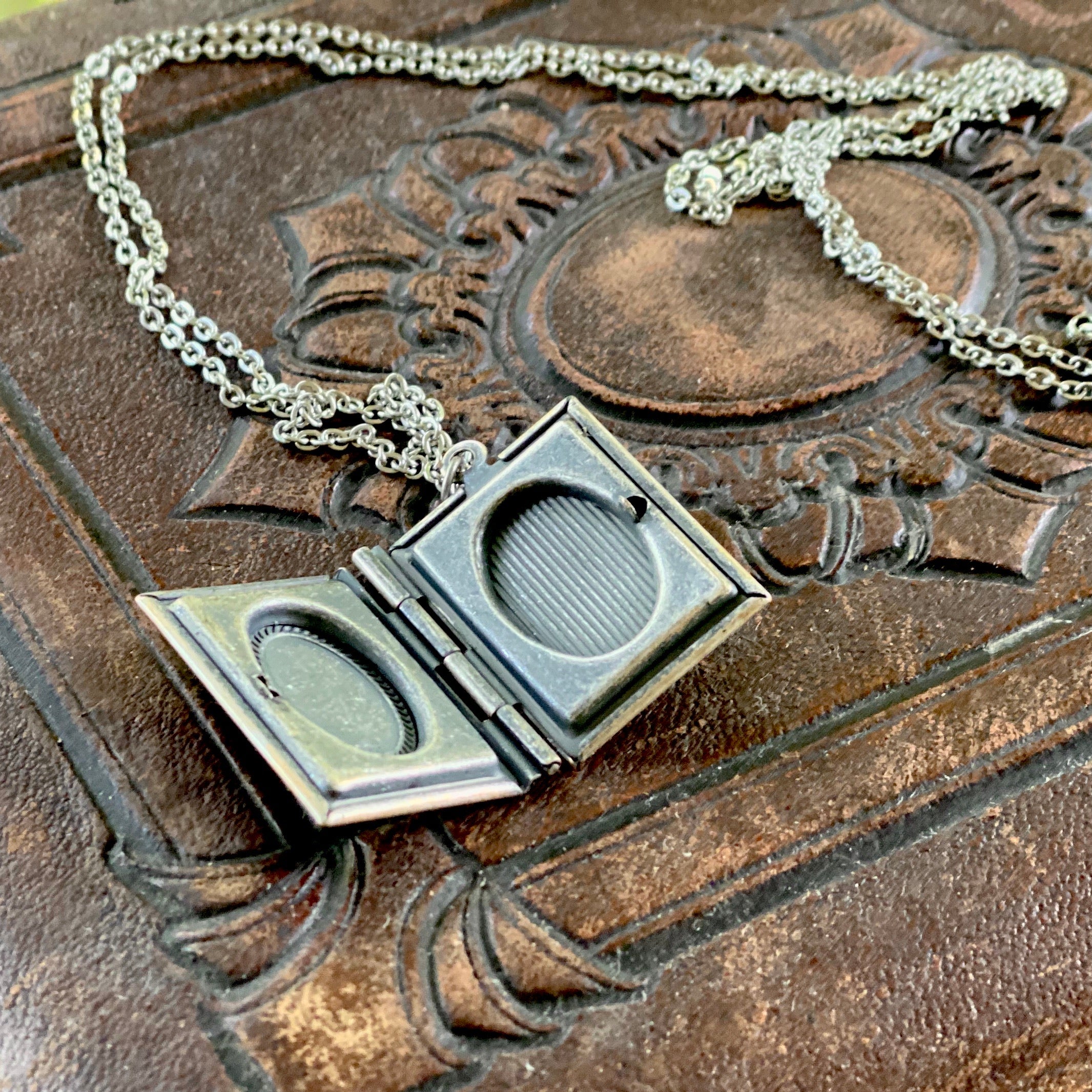 Open antiqued silver book locket with a small oval indent where a picture could be displayed.