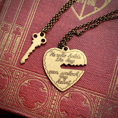 Antiqued brass necklaces. One with a key pendant and the other with a heart-shaped pendant with a key-shaped cutout. Heart pendant contains the quote: "He who holds the key can unlock my heart."