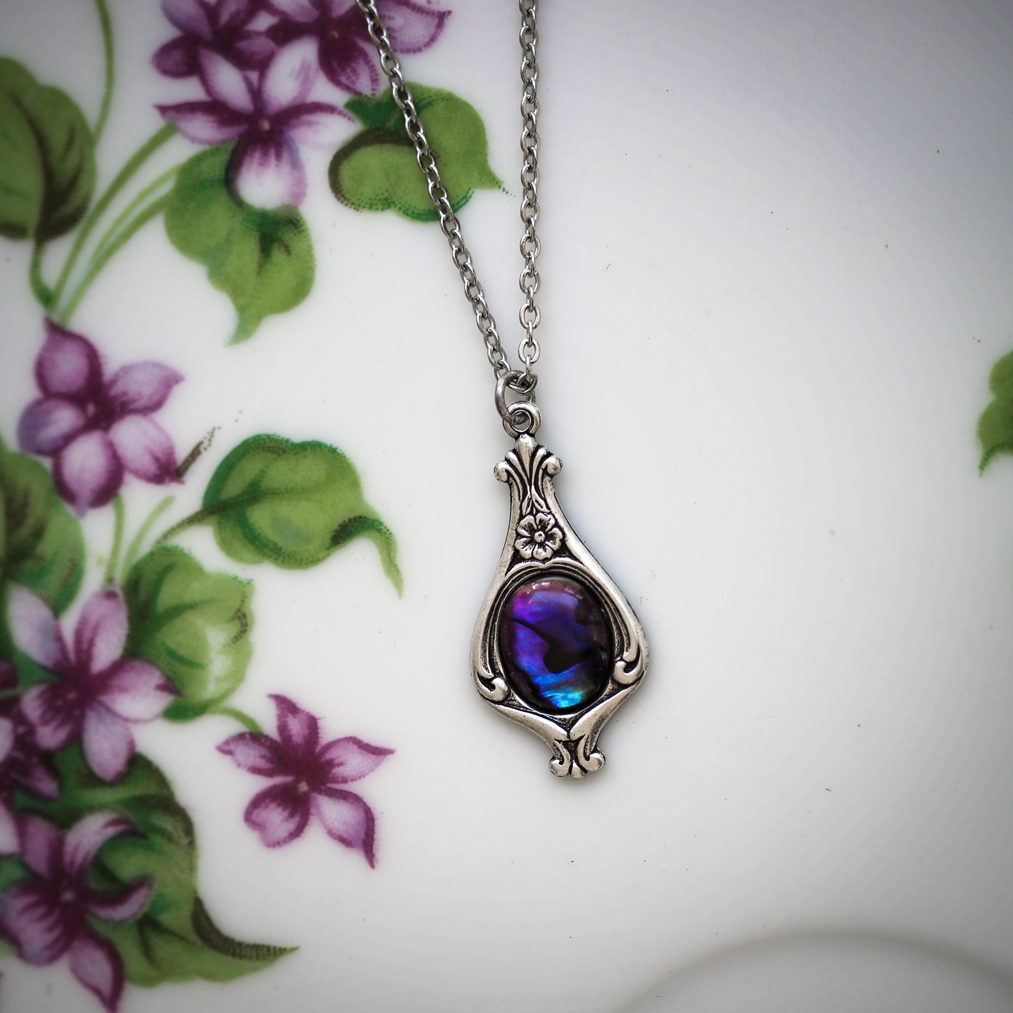 Antiqued silver vintage-inspired small dark nautical aesthetic necklace with a dainty purple blue paua shell on a mini floral drop setting.