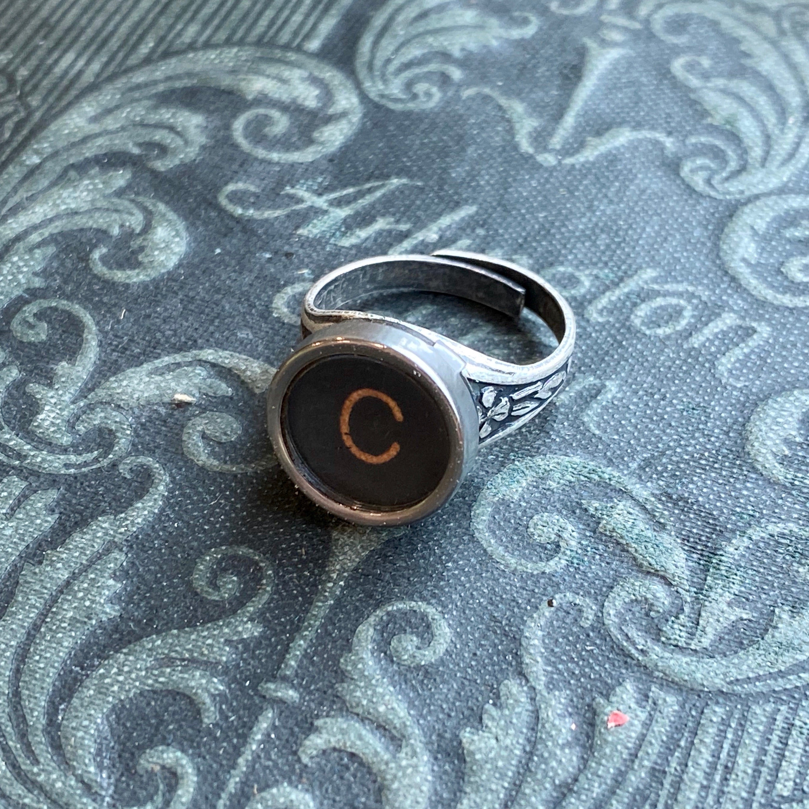Silver adjustable ring with an authentic vintage typewriter key as the centerpiece. The key is metal-rimmed with glass covering an off-white letter 'C' on a black background.