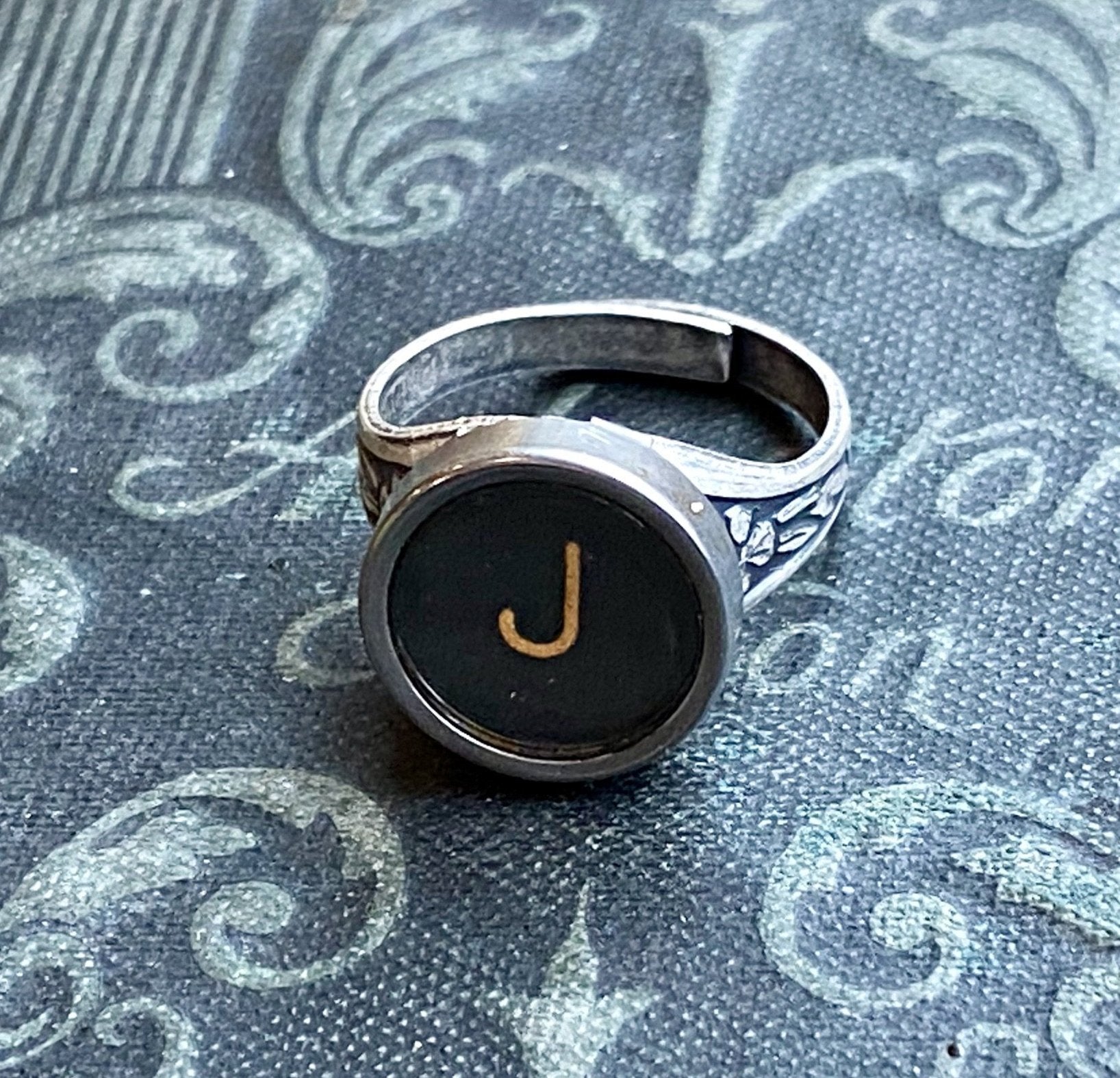 Silver adjustable ring with an authentic vintage typewriter key as the centerpiece. The key is metal-rimmed with glass covering an off-white letter on a black background.