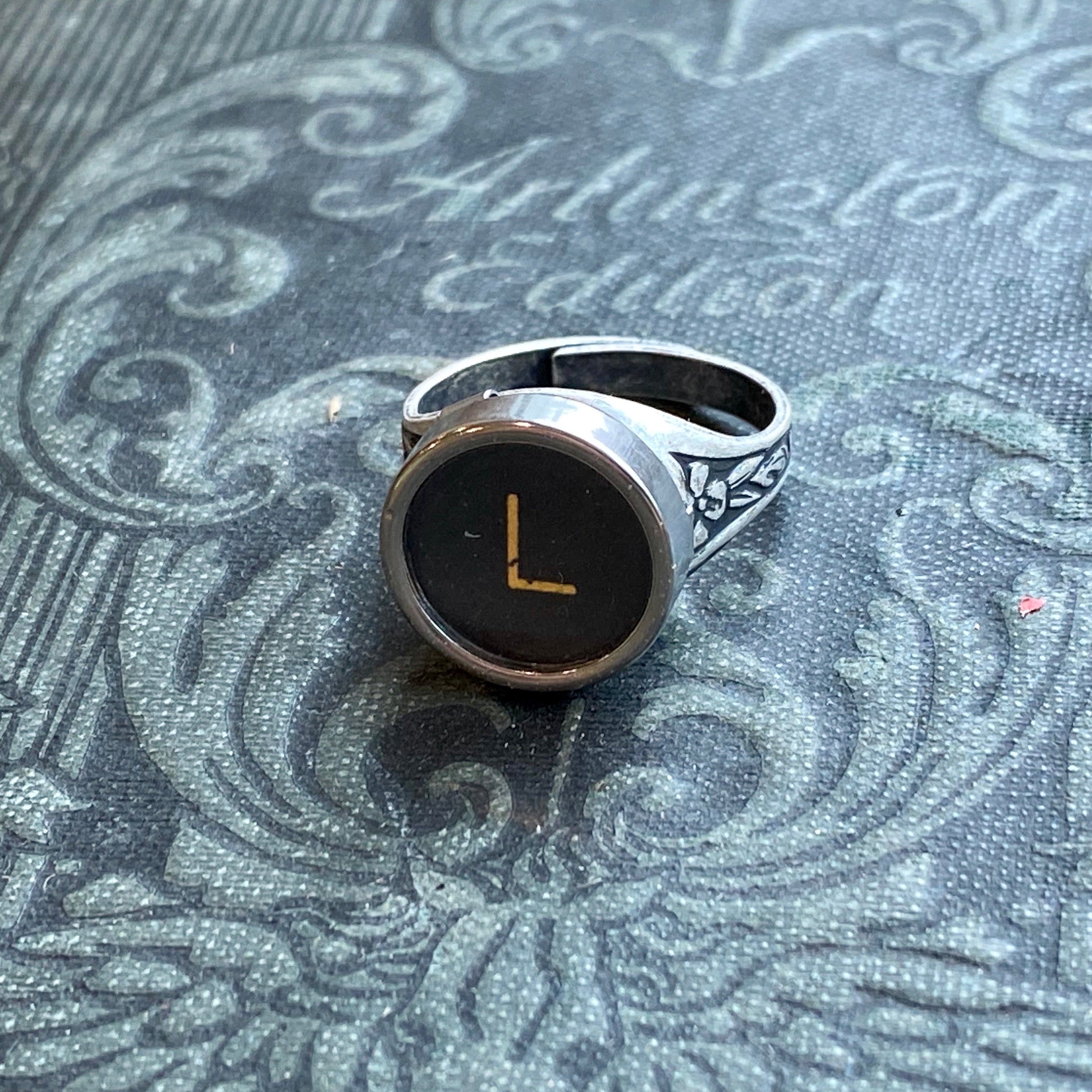 Silver adjustable ring with an authentic vintage typewriter key as the centerpiece. The key is metal-rimmed with glass covering an off-white letter 'L' on a black background.