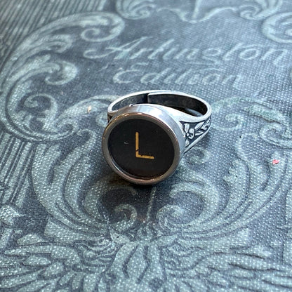 Silver adjustable ring with an authentic vintage typewriter key as the centerpiece. The key is metal-rimmed with glass covering an off-white letter 'L' on a black background.