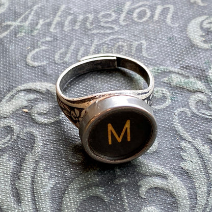 Silver adjustable ring with an authentic vintage typewriter key as the centerpiece. The key is metal-rimmed with glass covering an off-white letter 'M' on a black background.