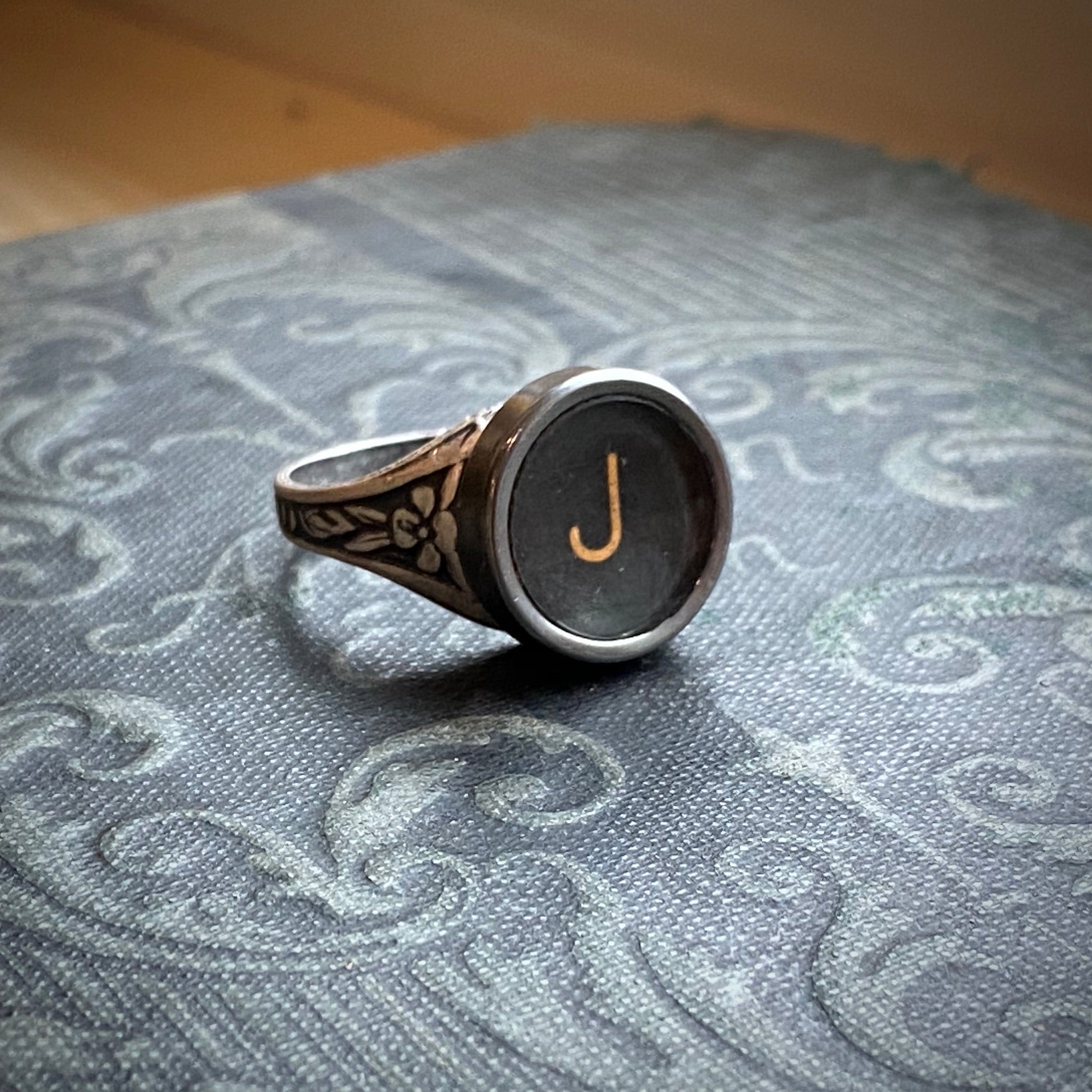Silver adjustable ring with an authentic vintage typewriter key as the centerpiece. The key is metal-rimmed with glass covering an off-white letter 'J' on a black background.