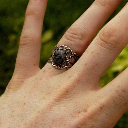 rich antiqued brass modern vintage inspired adjustable filigree ring with a dark black and gray mottled snowflake obsidian oval semi-precious mineral stone set in a medieval goth 
aesthetic
